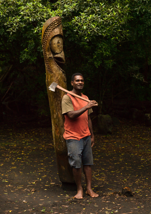 Ni-Vanuatu man with an axe in front of a slit gong drum in the jungle, Ambrym island, Olal, Vanuatu