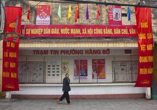 Veiled woman passing by propaganda posters of the communist party fenced with wire, Hanoi, Vietnam