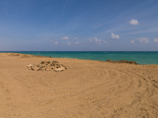Piled rocks mark a barren coastline beside a turquoise sea, Obock Region, Khor angar, Djibouti
