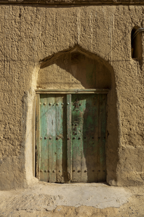 Weathered green wooden door set within an arched mudbrick doorway, Ad Dakhiliyah Region, Al Hamra, Oman