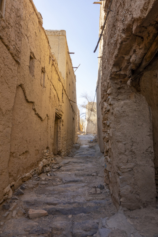 Empty narrow alley winding between weathered mudbrick houses toward distant buildings, Ad Dakhiliyah Region, Al Hamra, Oman