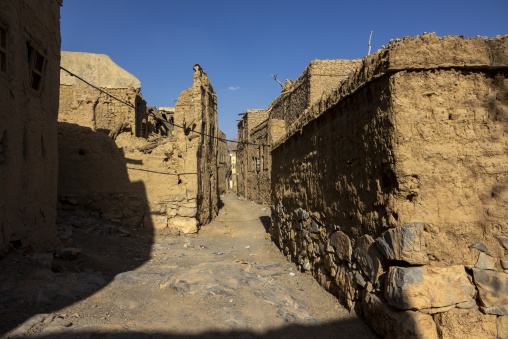 Narrow alley lined with ruined mudbrick walls leading toward distant buildings, Ad Dakhiliyah Region, Al Hamra, Oman