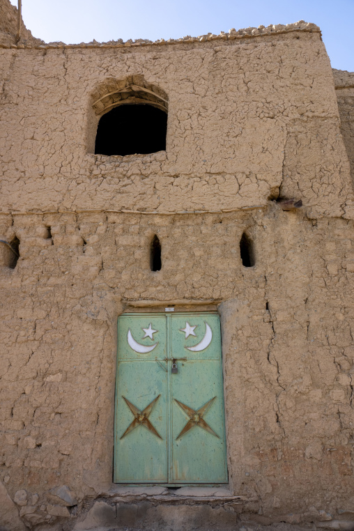 Green metal door decorated with crescent moon and star motifs set into a mudbrick facade, Ad Dakhiliyah Region, Al Hamra, Oman