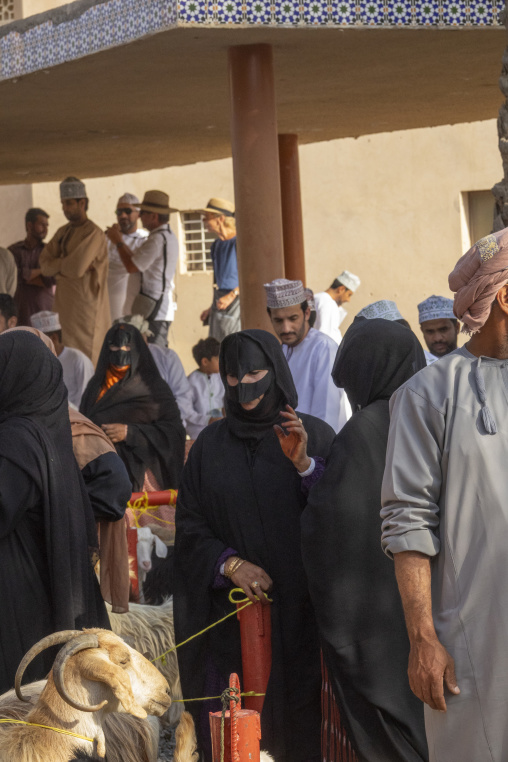 Crowd of Omani men and women gathered with a horned goat at the Nizwa Friday livestock market, Ad Dakhiliyah Region, Nizwa, Oman