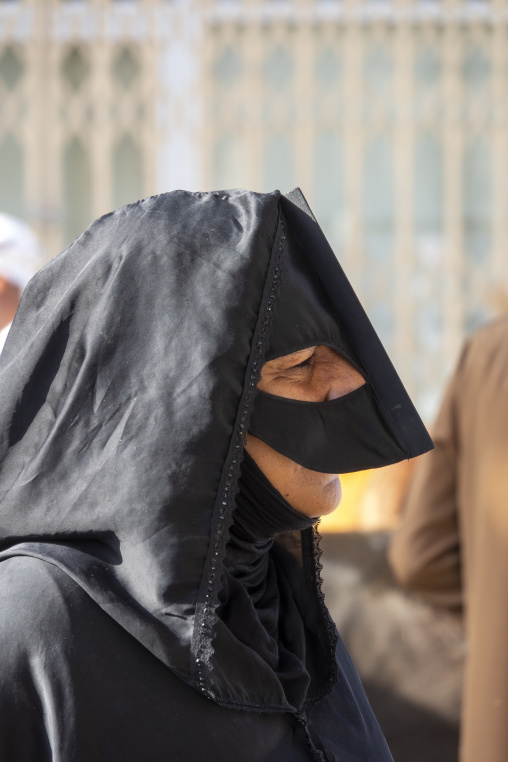 Close-up profile portrait of an elderly Omani woman wearing a black satin headscarf and traditional leather face mask, Ad Dakhiliyah Region, Nizwa, Oman