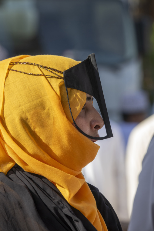 Close-up profile portrait of an Omani woman wearing a golden yellow headscarf and black leather face mask, Ad Dakhiliyah Region, Nizwa, Oman