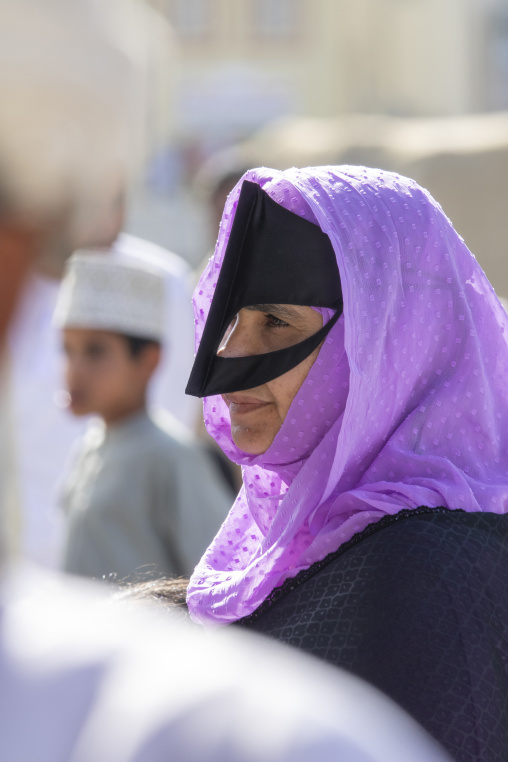Close-up profile portrait of a woman wearing a purple headscarf and a black traditional burqa face mask, Ad Dakhiliyah Region, Nizwa, Oman