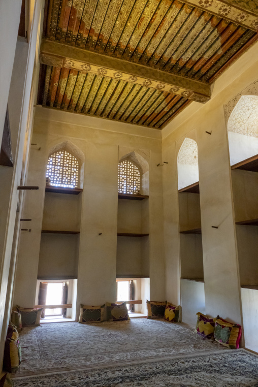 Interior of a traditional reception hall with painted wooden ceiling beams carved lattice windows and cushions along the walls, Ad Dakhiliyah Region, Nizwa, Oman