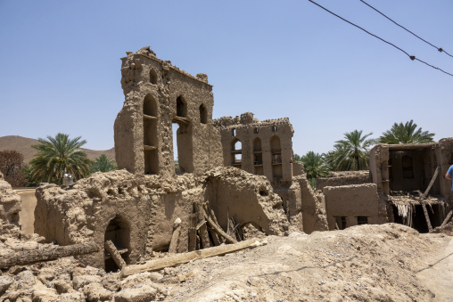 Ruined mudbrick building facade with tall arched window openings surrounded by palm trees, Ad Dakhiliyah Governorate, Birkat Al Mouz, Oman