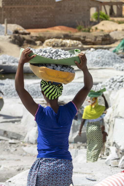 A woman lifts a basin of crushed granite onto her head at the quarry as others work behind her, Savanes district, Shienlow, Ivory Coast