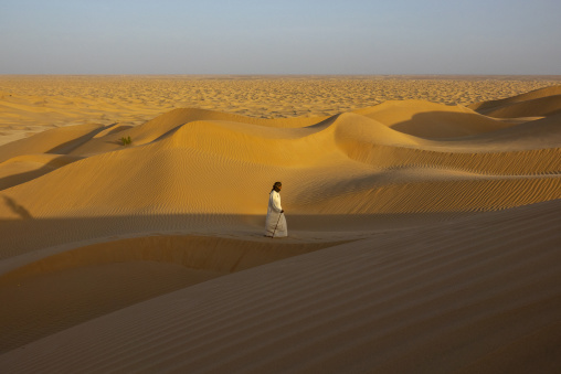 Man walking along a sand dune ridge overlooking a vast desert landscape, Dhofar Governorate, Rub al Khali, Oman