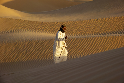 Portrait of a laughing man wearing a headscarf and white robe standing on a sand dune ridge, Dhofar Governorate, Rub al Khali, Oman