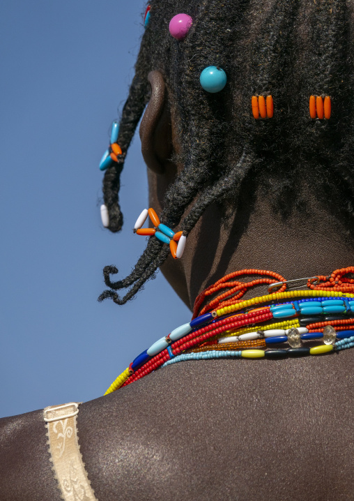Close-up of braided hair decorated with colorful beads above layered necklaces on a woman's shoulder, Cunene Province, Cahama, Angola