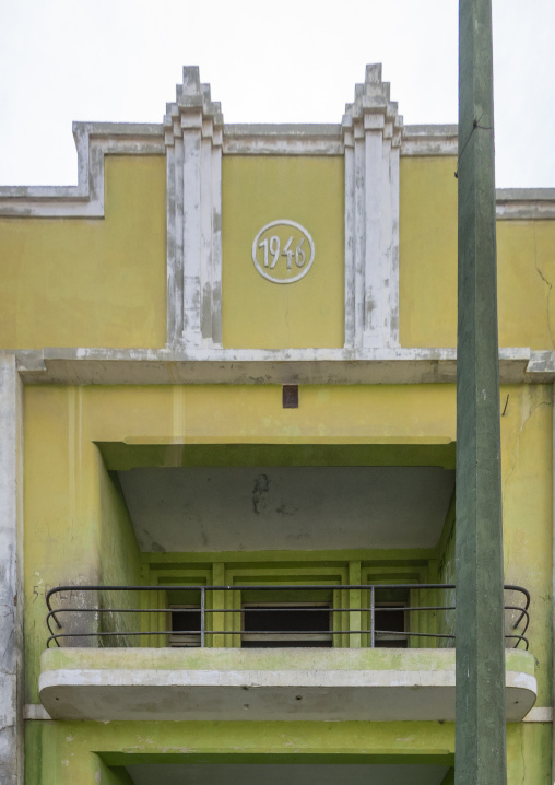 Weathered yellow Art Deco building facade featuring a 1946 date medallion above a balcony, Namibe Province, Namibe, Angola