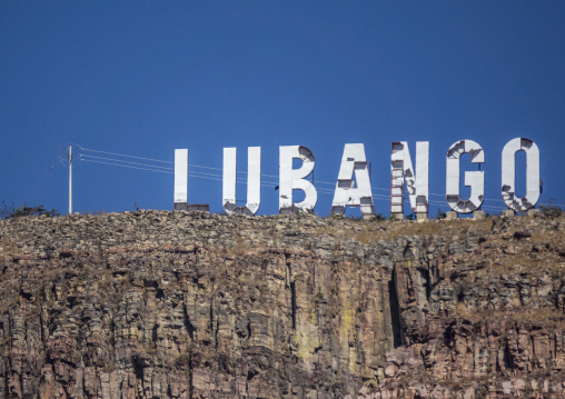 Large white LUBANGO sign standing atop a rocky cliff against a blue sky, Huila Province, Lubango, Angola