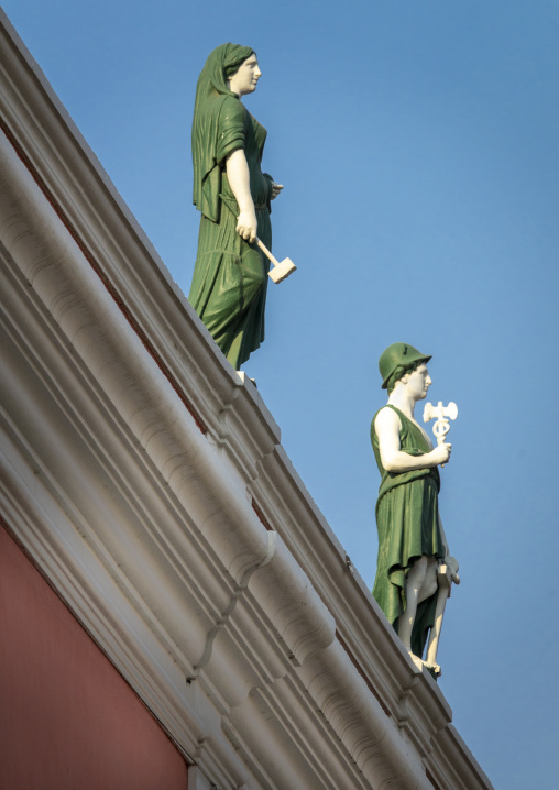 Two allegorical statues holding a hammer and a caduceus stand on the roof cornice of a historic building, Luanda Province, Luanda, Angola
