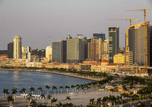 Palm-lined promenade curves along Luanda Bay beneath a skyline of modern towers and a colonial red-domed building, Luanda Province, Luanda, Angola
