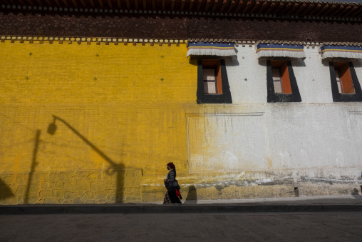 Tibetan woman walking along a monastery's colorful outer wall, Tongren County, Longwu, China